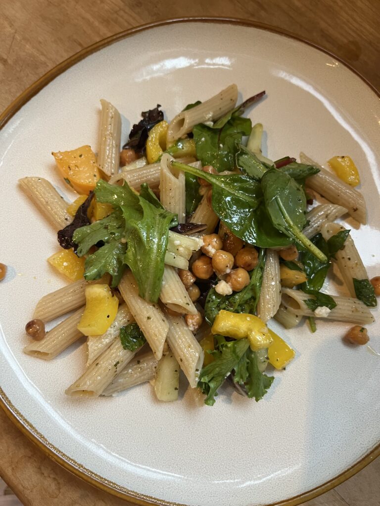 pasta salad example on a plate with chickpeas, yellow peppers, feta cheese, cucumbers, and salad greens.